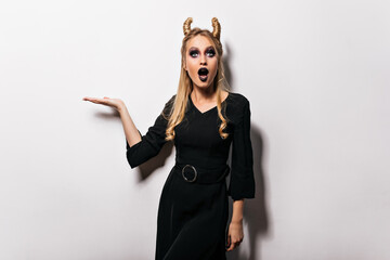 Cheerful blonde girl with black makeup posing in halloween. Studio photo of fascinating female...