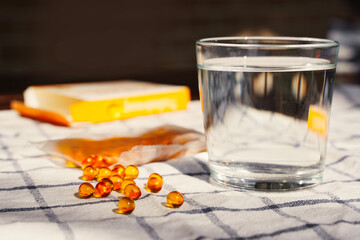 Fish oil capsules and glass of water on the table. Cod liver oil, omega-3. Nutritional supplements. Sport, diet concept.