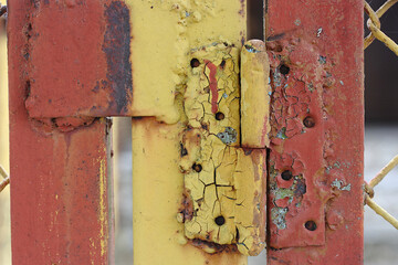 Old yellow and brown paint on a door hinge on a metal bar