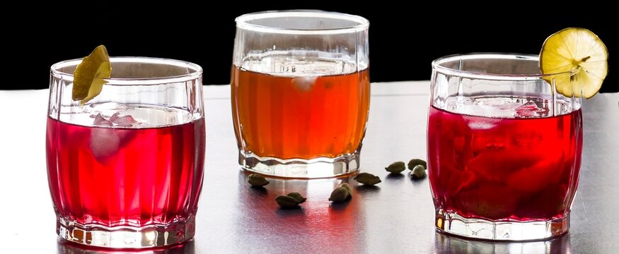 Front view and close up of three glasses of Sangria fruit punch,topped with lime.Cold summer drink or mocktail variety with kokam,strawberries,citrus fruits kahwa. Isolated on dark wood background.
