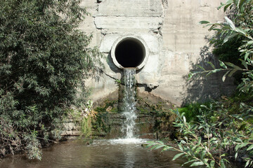Sewage or sewage water flows out of the drain pipe into the river - obrazy, fototapety, plakaty