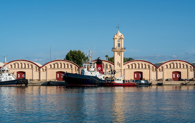 Fototapeta na wymiar Boats in front of warehouses and lighthouse at the port of Gandia, Spain
