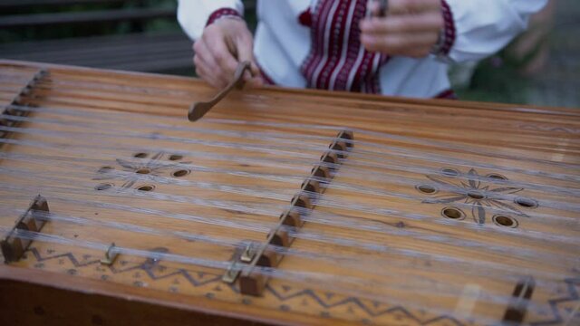 Caucasian man in embroidered shirt plays dulcimer. Man knocks special hammers on stretched strings on wooden board and plays traditional music. Stringed percussion musical instrument sounds good