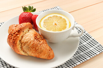 croissant with nuts on the plate with cup of lemon tea on the wooden background