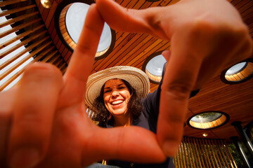 A young beautiful woman in a hat makes a frame out of her fingers, creatively takes selfies with a...