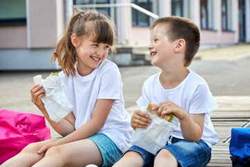 Schoolchildren boy and girl laugh and eat their lunch, snack, breakfast in the school yard. Food...