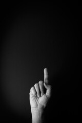 Black and white image of hand demonstrating sign language number one against black background with empty copy space