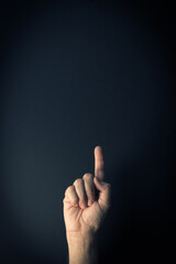 Colour image of hand demonstrating sign language number one against dark background with empty copy space