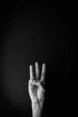 Black and white image of hand demonstrating sign language number three against black background with empty copy space