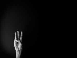 Black and white image of hand demonstrating sign language number three against black background with empty copy space