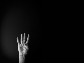 Black and white image of hand demonstrating sign language number four against black background with empty copy space