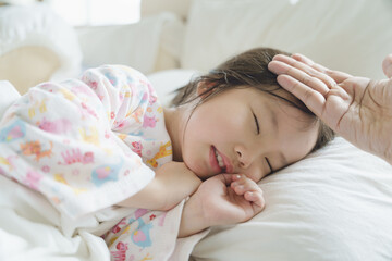 Obraz premium Parent put the hand on forehead of sleeping toddler to check fever temperature while the kid got sickness in the bed.