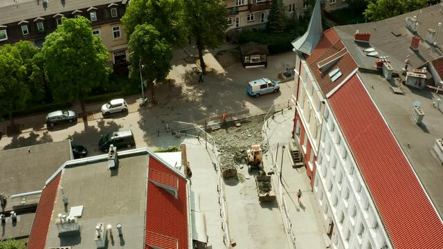 Aerial view of the street of the old city and a small excavator digging paving stones and loading it into a dump truck. Repair of the road and laying of new paving stones and a curb in the old city.