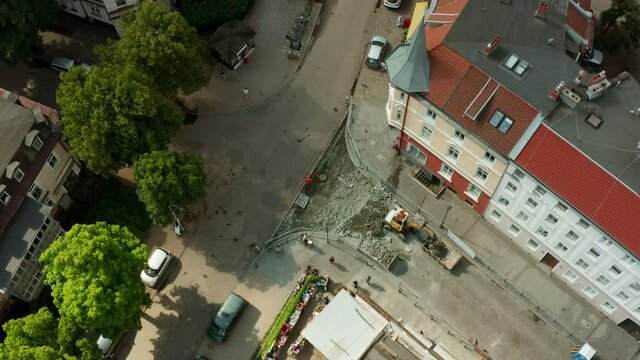 Aerial view of the street of the old city and a small excavator digging paving stones and loading it into a dump truck. Repair of the road and laying of new paving stones and a curb in the old city.