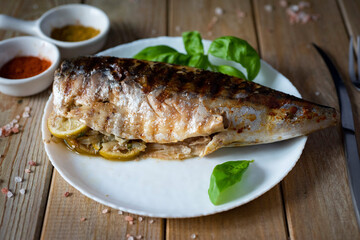 Fish dish: grilled mackerel stuffed with vegetables and lemon on a white plate on a wooden table. Close-up