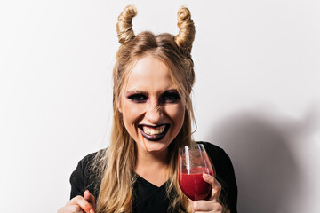 Close-up shot of cheerful girl drinking blood in halloween. Carefree vampire with blonde hair posing at carnival.