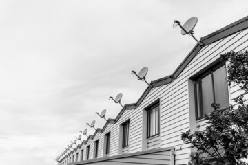 Long row of repeating gables and television dishes on small city apartments from street