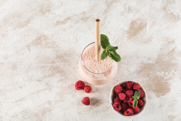 A glass with a Lassi drink with raspberries, mint and a bamboo tube on a light background.