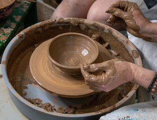The female hands of a master potter form an earthen vessel on a potter's wheel. A potter works in a pottery workshop with clay. Close-up.