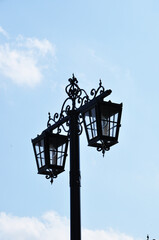 Lighting post. Two lanterns of the lighting pole against the background of the blue sky. Figured design of the lighting column.