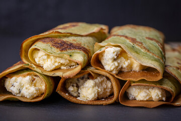 Homemade pancakes with green spirulina stuffed white cottage cheese with raisins on a black slate background