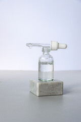 Bottle of natural skincare lotion with pipette on podium on light grey background. Trendy selfcare products. Front view