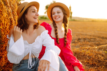 Two smiling young woman resting near haystack. Fashion concept. Nature, vacation, relax and lifestyle.