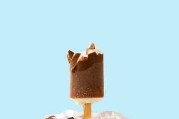 Close up view of bitten off ice cream in chocolate glaze on blue background.