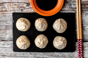 Dim Sum, traditional Japanese food, served on a black slate plate, with a bowl of soy sauce and some chopsticks, on a rustic wooden background.