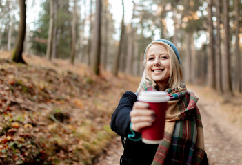 Beautiful blond girl in blue hat with cup of coffee in a forest