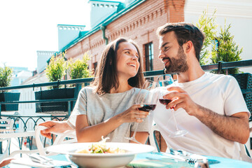 Smiling beautiful woman and her handsome boyfriend. Happy cheerful family. Couple cheering with glasses of red wine at their date in restaurant. They drinking alcohol at veranda cafe in the street