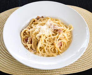 spaghetti carbonara in white plate on straw mat