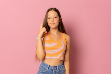 Portrait of a happy girl wearing casual clothes pointing finger up at copy space isolated over pink background