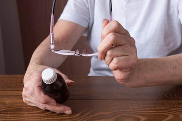 elderly woman holds a bottle of medicine, using glasses to read the instructions on the package...
