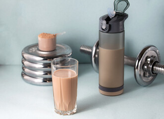 Sports nutrition concept. Coffee-colored protein is poured into a cube, a finished drink is poured into a glass glass, next to a shaker and a metal dumbbell. Horizontal orientation.