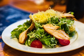 Caesar salad with pieces of fried chicken. Greens, tomatoes, sauce.