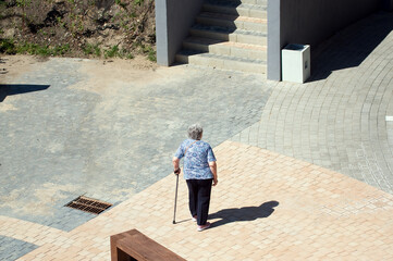 Starsza kobieta o lasce stojąca na kamiennym  placu