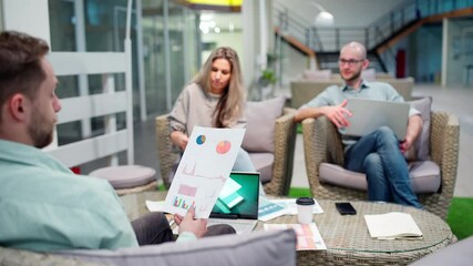 Startup team of three sitting in office lobby and discussing business strategy. Manager explaining market research stats and presenting printout to colleagues at meeting, focus on document