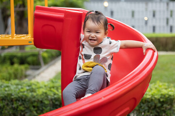 Asian Baby Girl Playing on a Red Slider on the Playground