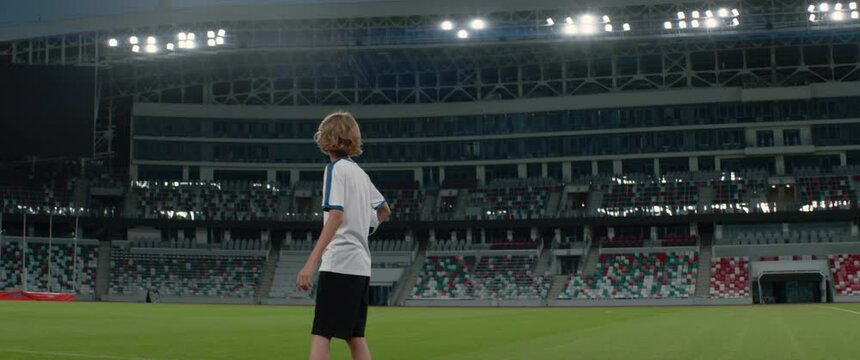 Portarit of Caucasian pre teen kid boy entering the field of huge soccer stadium, holding a ball, dreaming of becoming professional player, soccer star