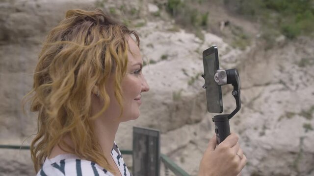Beautiful woman takes pictures on phone with steadicam. Action. Young woman takes pictures on phone with manual stabilizer. Traveler takes pictures on hand-held steadicam in mountains