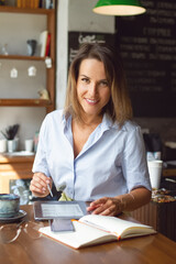 Portrait of businesswoman with e-book and diary, smartphone and coffee works remotely in cafe