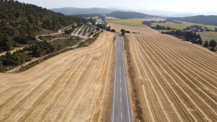 Larga arretera de montaña entre campos cosechados de cebada y trigo