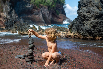 Boy kid building stone stack on pebble beach.