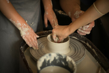 a child and an adult rotate the clay on a potter's wheel