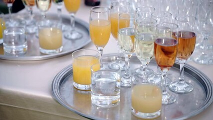 Silver trays with glasses of champagne, fizzing white wine and fresh juice prepared for guests at banquet table outdoors. Luxury beverages at celebration party, catering service and buffet concept - Powered by Adobe