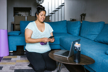 Curvy latin girl using smartphone kneeling in living room in Latin America, plus size woman