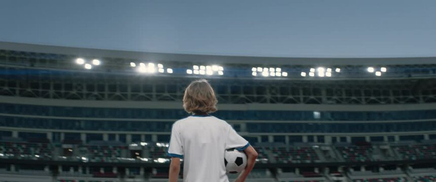 Portarit of Caucasian pre teen kid boy entering the field of huge soccer stadium, holding a ball, dreaming of becoming professional player, soccer star