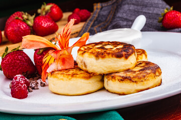Breakfast. Cottage cheese pancakes, syrniki, curd fritters with fresh berries raspberry and strawberry, sour cream on white plate. Russian or Ukrainian cuisine.