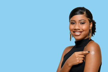 black teenage girl smiling happily and showing the vaccine mark on her arm, isolated on blue background - obrazy, fototapety, plakaty